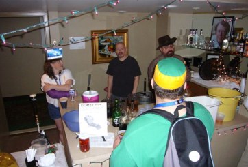 Minicon 42 bar, the bar itself, with three people behind the bar and one person in front. Lights dangle about.