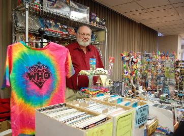 A dealer at Minicon 42 who is selling lots of stuff, notably a tie-dye Dr. Who t-shirt