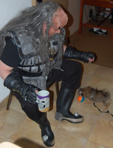 Photo by Ben Huset: A Klingon with a skull mug at a room party at Minicon 42 looking down at a very small fluffy dog named Chewy